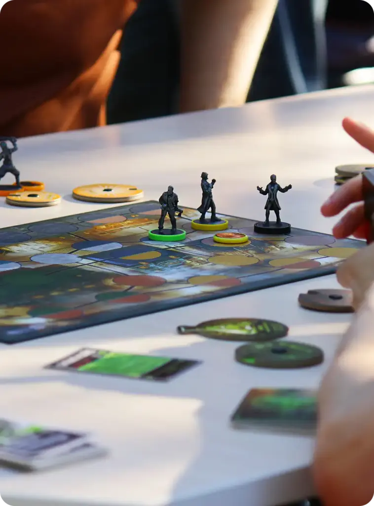 Közelkép a játékosokról, akik miniatűröket és kártyákat mozgatnak a stratégiai társasjáték asztalán egy asztali játék során.