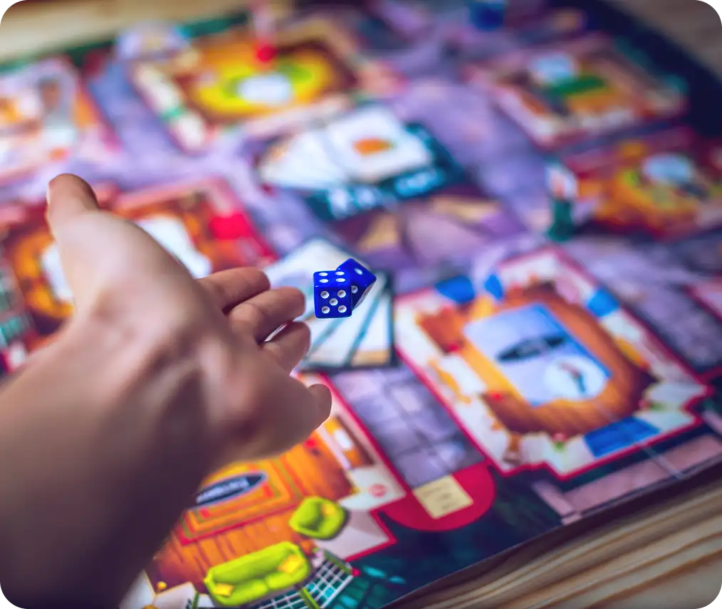 Kézzel kék kockát dobnak színes társasjáték felállítása felett az asztalon